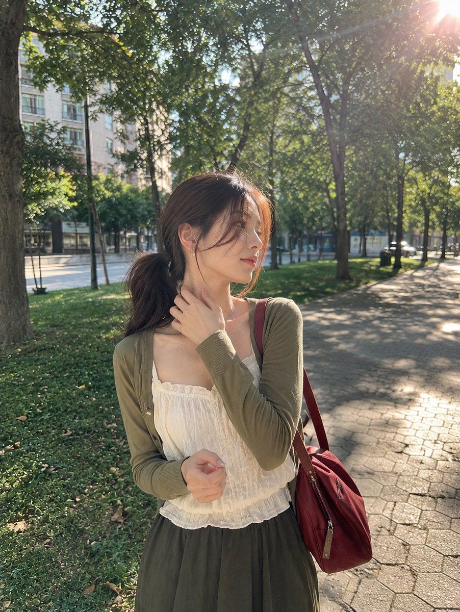 一张照片般逼真的抓拍户外肖像，画面中一位年轻女子在晴朗的午后站立于宁静的城市公园。她留着一头深棕色长发，梳成松散的低马尾，几缕纤细的碎发轻柔地垂落在脸庞两侧…