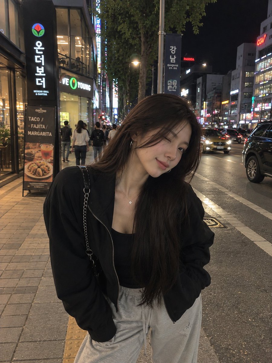 一张照片级写实风格的夜间街头人像照,一位年轻女子在繁华的韩国城市街区中随意地自拍。她留着长而顺直的黑发,妆容柔和自然,佩戴着低调的环形耳环和一条精致的项链。她…