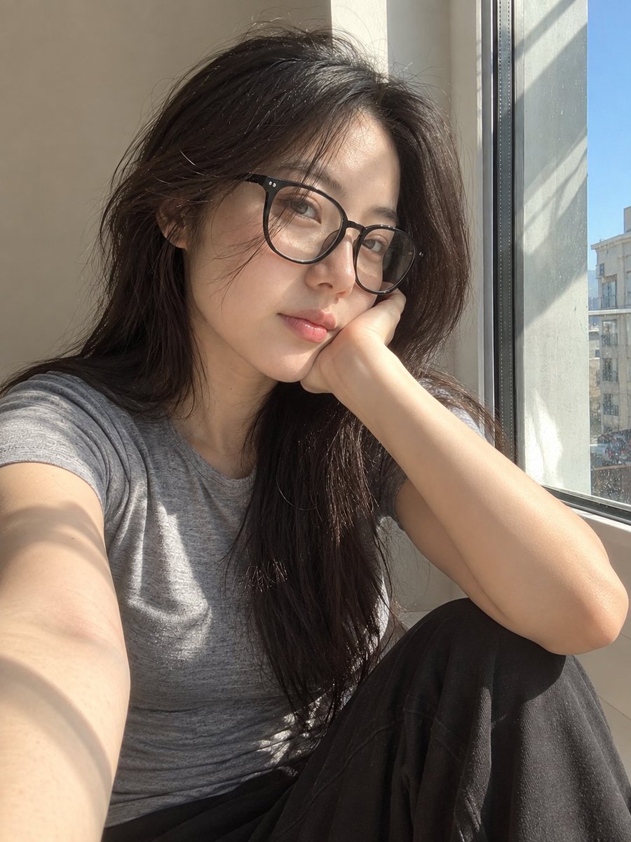 超写实风格的休闲智能手机自拍照：一位年轻东亚女性坐在安静房间内靠近阳光照射的窗户旁。保持与面部参考的高度相似性，包括柔和轮廓的鹅蛋脸、温和的下颌线、自然比例的鼻子、真实的唇形、均…