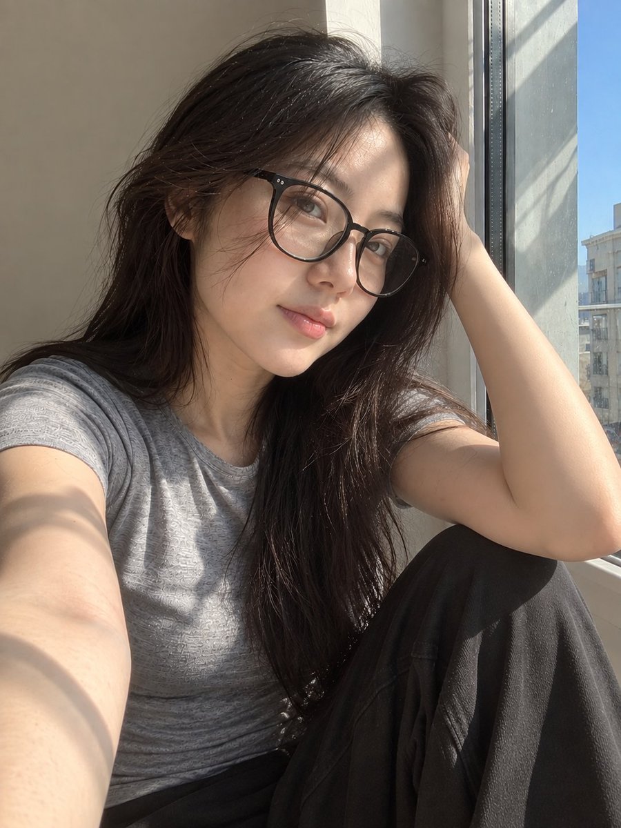 超写实风格的休闲智能手机自拍照：一位年轻东亚女性坐在安静房间内靠近阳光照射的窗户旁。保持与面部参考的高度相似性，包括柔和轮廓的鹅蛋脸、温和的下颌线、自然比例的鼻子、真实的唇形、均…