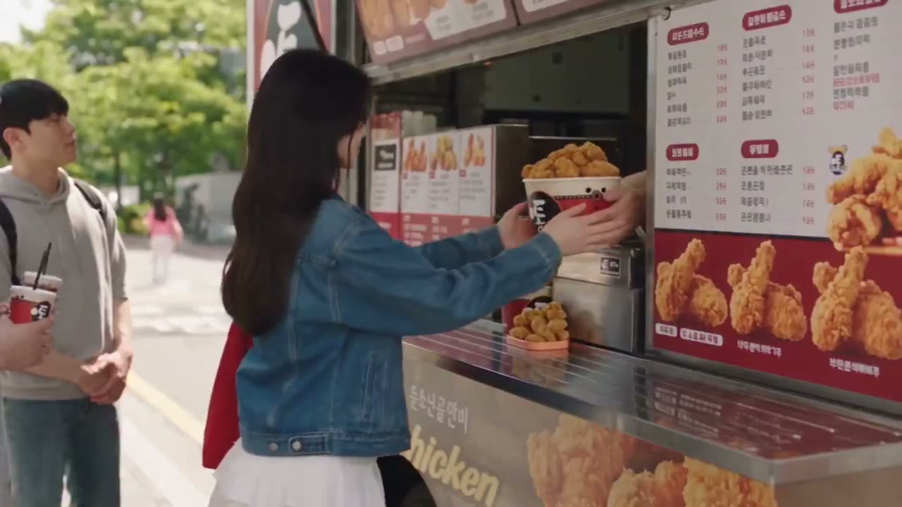 一位年轻亚裔女性身穿牛仔外套和白裙，在阳光明媚的街道上从一辆美食餐车购买一桶酥脆炸鸡。当她转身离开时，脚下一滑，将整桶炸鸡抛向空中。镜头近距离推近，捕捉悬停在…