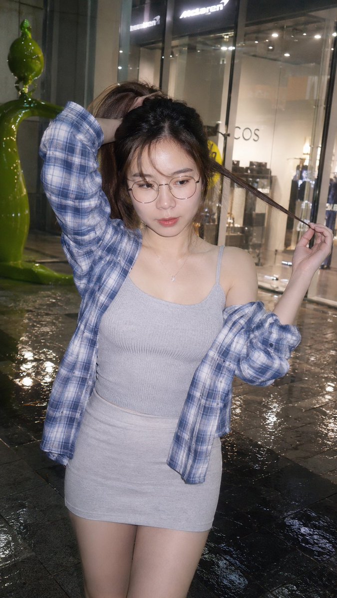 真实感抓拍闪光灯胶片街头快照,中国网络红人,惊艳美人,瓷器般冷调白皙肌肤,深棕色长马尾搭配空气感透薄刘海,精致的鹅蛋脸,薄框圆眼镜后的大眼睛清澈无辜,水润光泽…